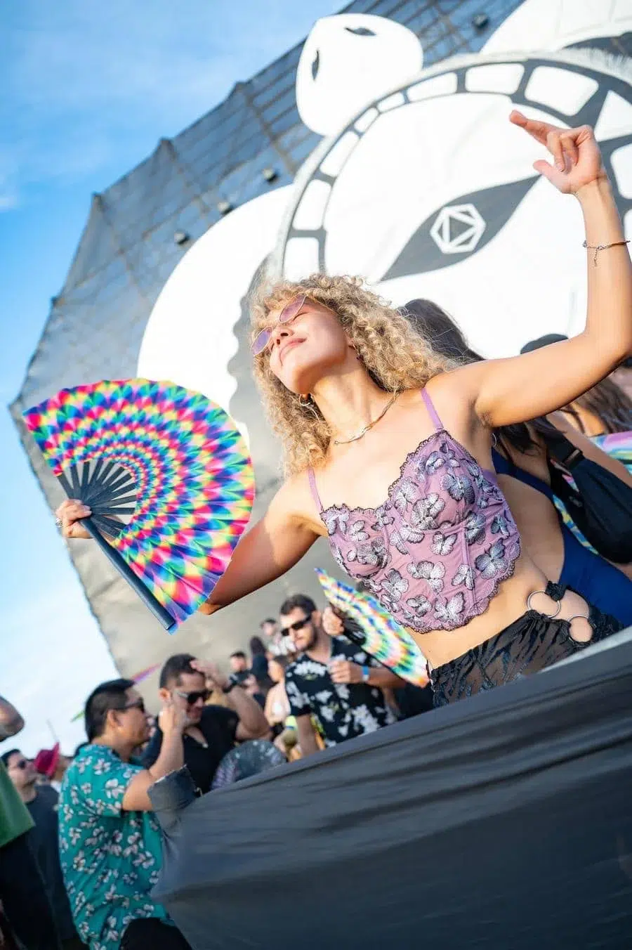 Woman dancing with a colorful folding fan at a daytime outdoor festival event.