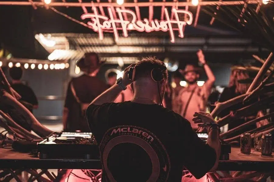 festivals in costa rica-26 | Pacific Photography DJ wearing headphones at a mixing desk in a dim nightclub, crowd dancing under pink neon lights.
