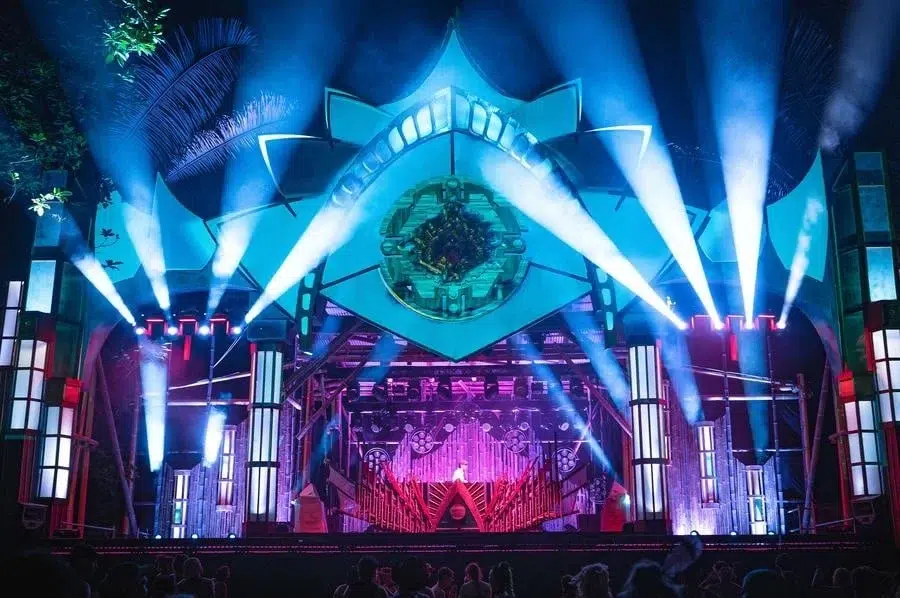 festivals in costa rica-3 | Pacific Photography Nighttime concert stage with blue laser beams, tall illuminated pillars, and a circular eye-like centerpiece above the performer. Audience silhouettes in front.