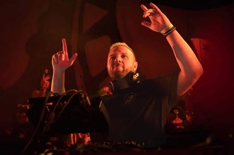 festivals in costa rica-32 | Pacific Photography DJ behind a mixer in red club lighting, hands raised as he cues the beat, wearing headphones on his neck.