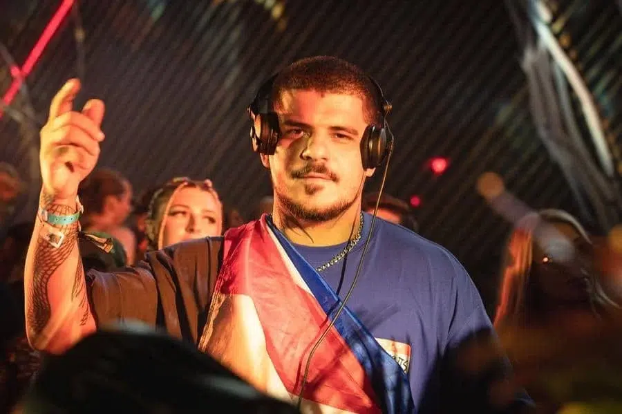 festivals in costa rica-35 | Pacific Photography DJ wearing headphones and a flag draped over his shoulder, raising a hand at a crowded club.