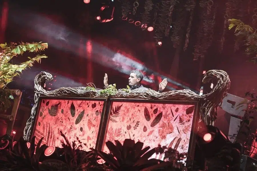 festivals in costa rica-4 | Pacific Photography DJ performing behind an ornate dragon-themed booth with red lighting and surrounding plants in a club setting, hands raised.