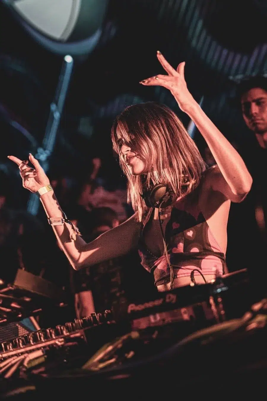 DJ wearing headphones performs on stage with arms raised during a nighttime set at a club.