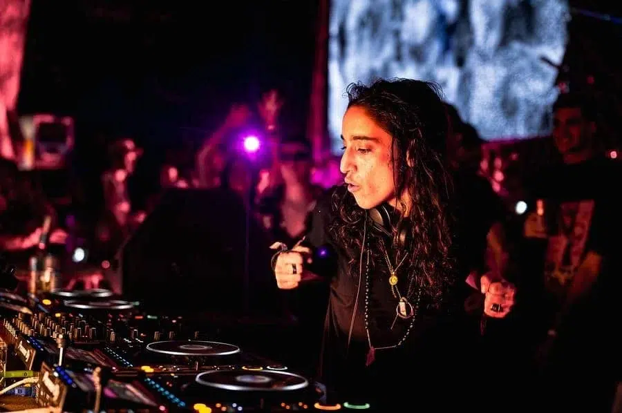 festivals in costa rica-65 | Pacific Photography Female DJ with long dark hair performing at a club, hands on the mixer with colorful stage lights and a crowd in the background.