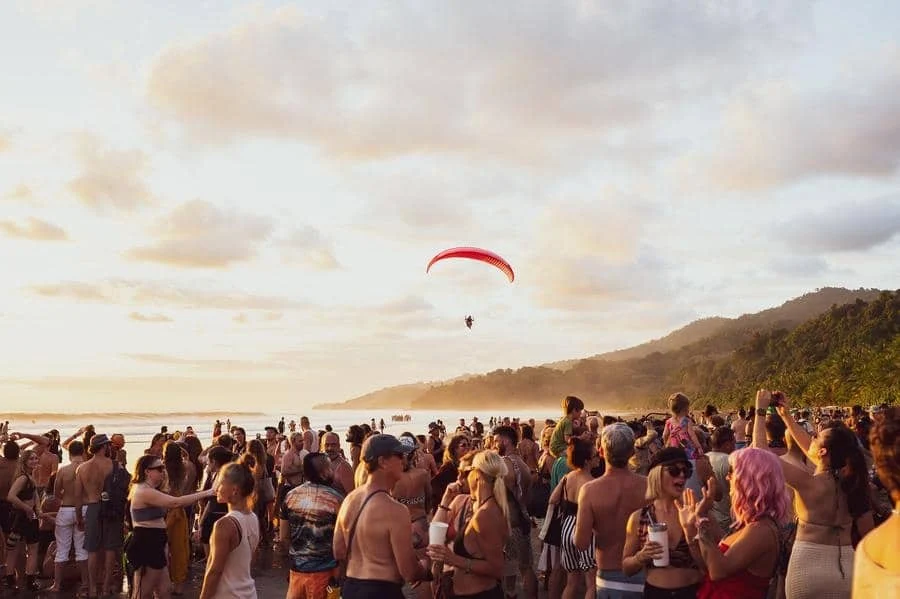 festivals in costa rica-7 | Pacific Photography Crowd of people on a beach at sunset with a red paraglider overhead and hills in the distance.