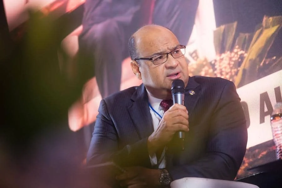 brands business and corporate photography -10 | Pacific Photography Man in a dark suit and glasses speaks into a microphone at a conference or panel discussion.