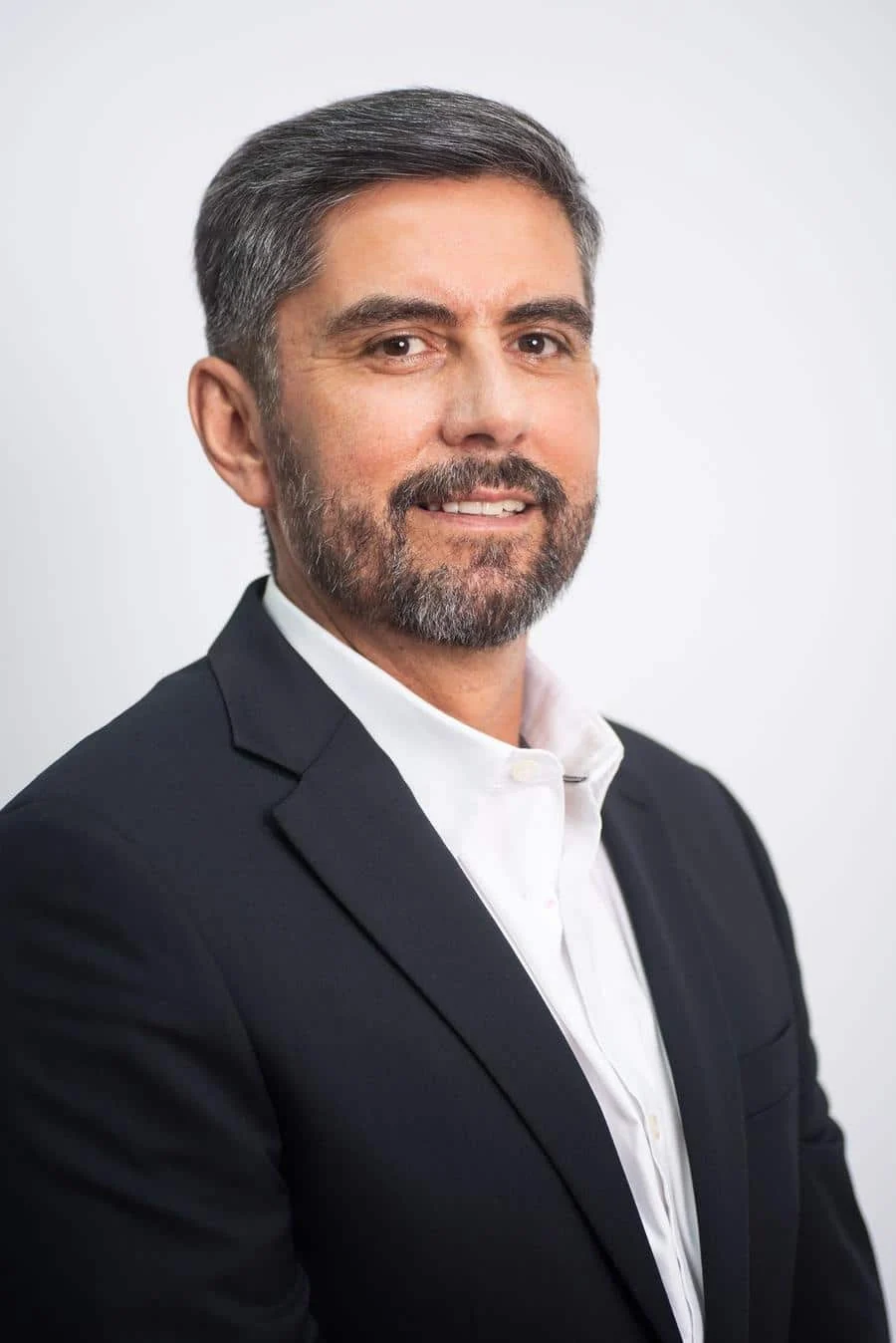 brands business and corporate photography -11 | Pacific Photography Portrait of a middle-aged man in a dark blazer and white shirt, smiling, against a light neutral background.