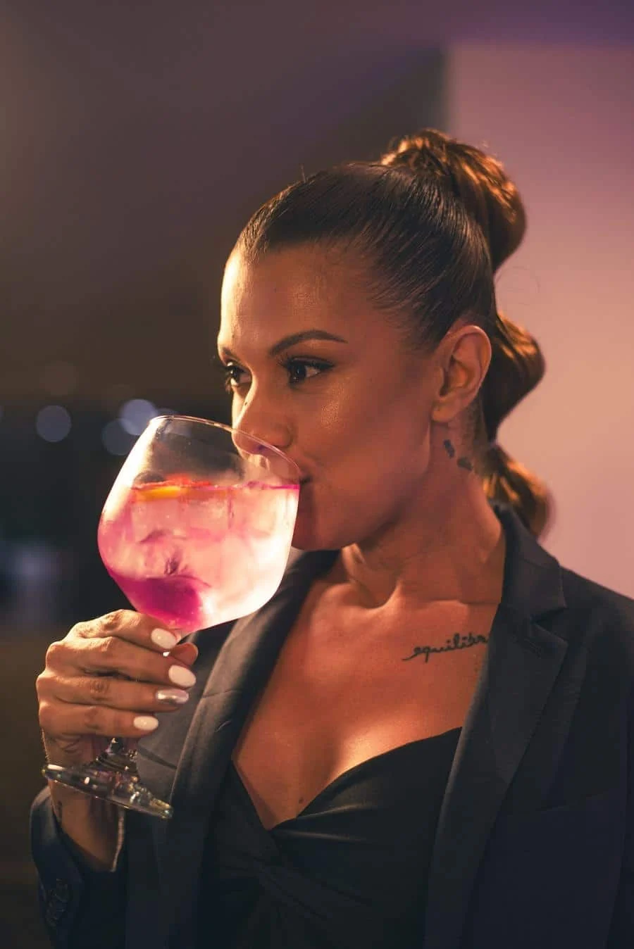 brands business and corporate photography -14 | Pacific Photography Woman in a blazer sipping a pink cocktail from a large stemmed glass with ice.