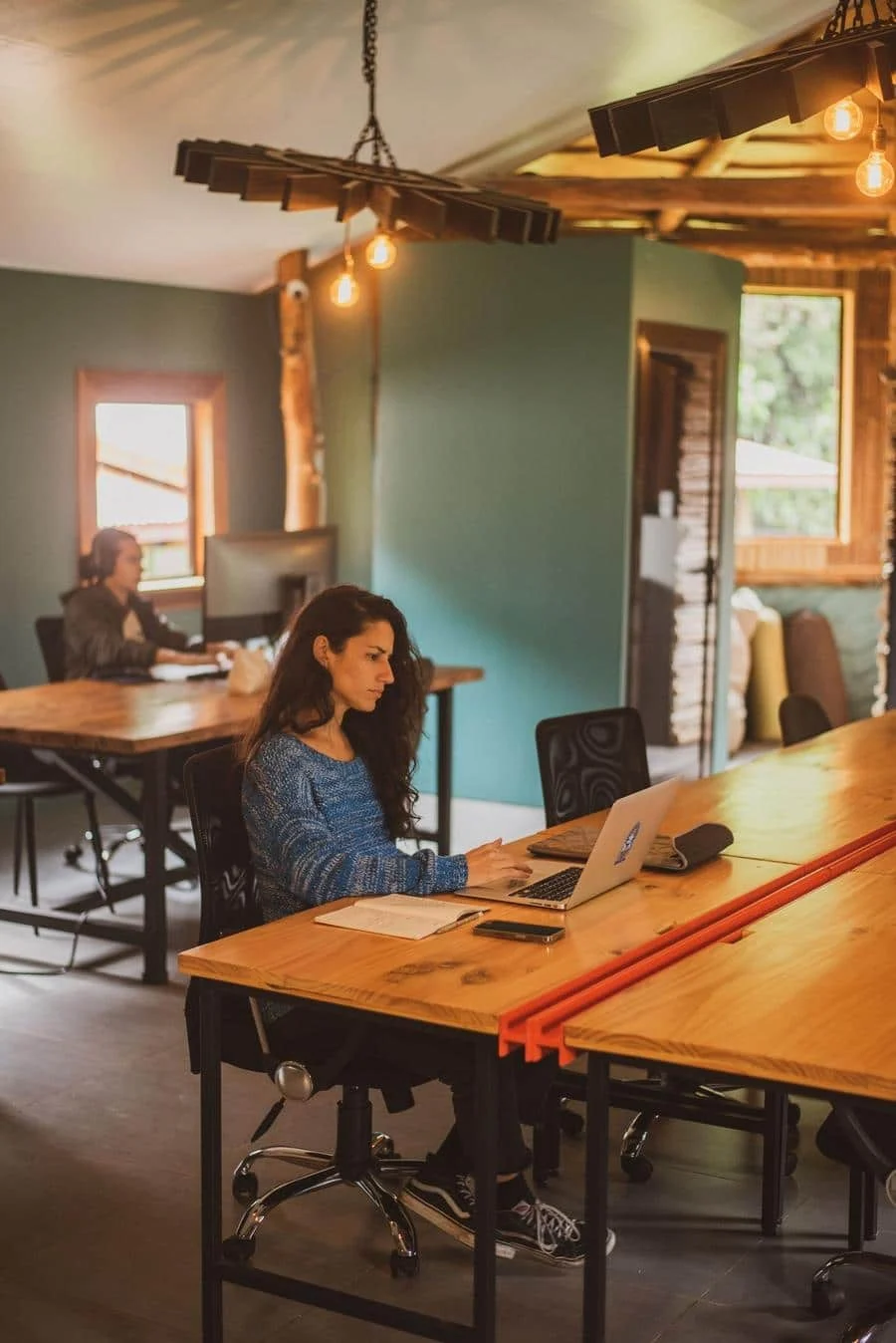 brands business and corporate photography -15 | Pacific Photography Woman with long dark hair typing on a laptop at a wooden desk in a bright, rustic coworking space.