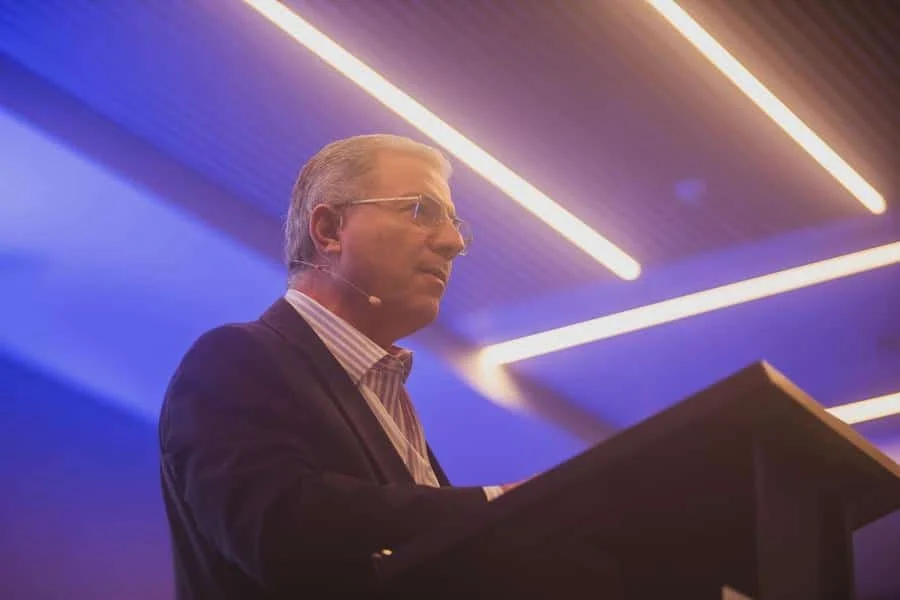 brands business and corporate photography -19 | Pacific Photography Man in a suit delivering a lecture at a podium with a headset microphone under purple stage lighting.