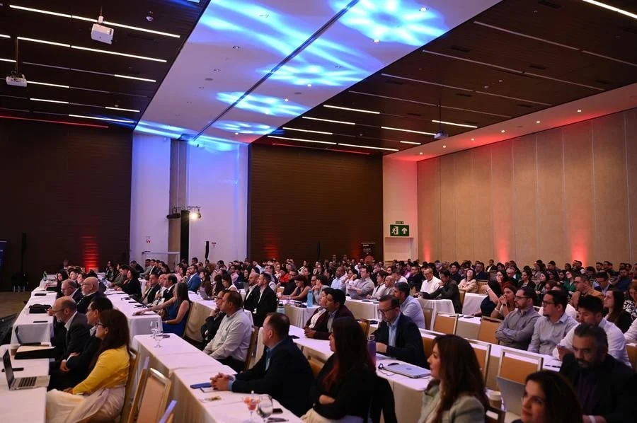 brands business and corporate photography -21 | Pacific Photography Audience seated in a large conference hall listening to a presentation, with white-clothed tables and blue/red lighting overhead.