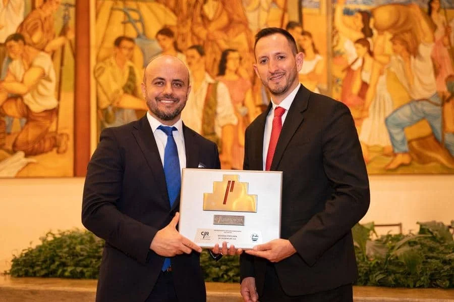 brands business and corporate photography -22 | Pacific Photography Two men in suits hold a framed award and smile at the camera at a formal ceremony, with a mural behind them.