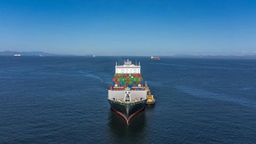 brands business and corporate photography -23 | Pacific Photography Container ship carrying colorful shipping containers sails in calm blue ocean, viewed from above with distant ships on the horizon.