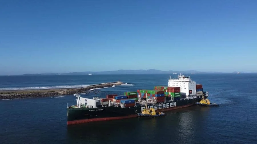 brands business and corporate photography -24 | Pacific Photography Container ship with stacked colorful containers being guided by yellow tugboats near a breakwater.