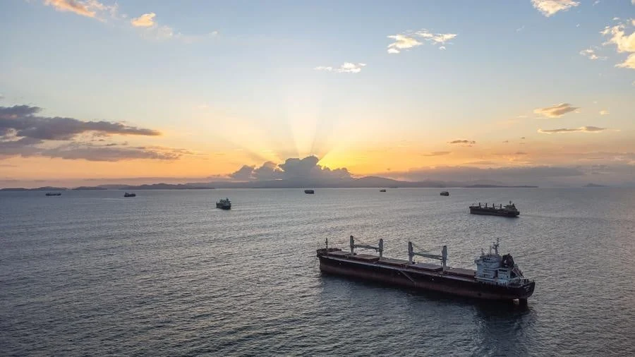 brands business and corporate photography -27 | Pacific Photography Sunset over calm sea with several cargo ships, the horizon glowing with orange light and sun rays breaking from clouds.