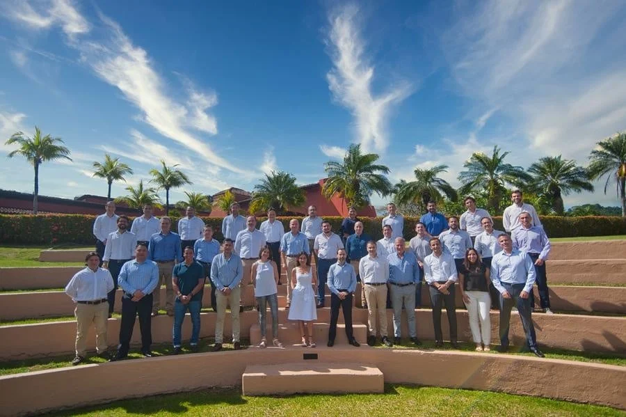 brands business and corporate photography -28 | Pacific Photography Group of professionals posing on terraced steps outdoors under a blue sky with palm trees, likely a team photo.