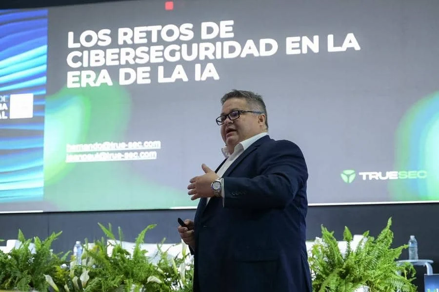 brands business and corporate photography -31 | Pacific Photography Speaker in a dark suit presenting on stage with a large screen behind reading 'LOS RETOS DE CIBERSEGURIDAD EN LA ERA DE LA IA'.