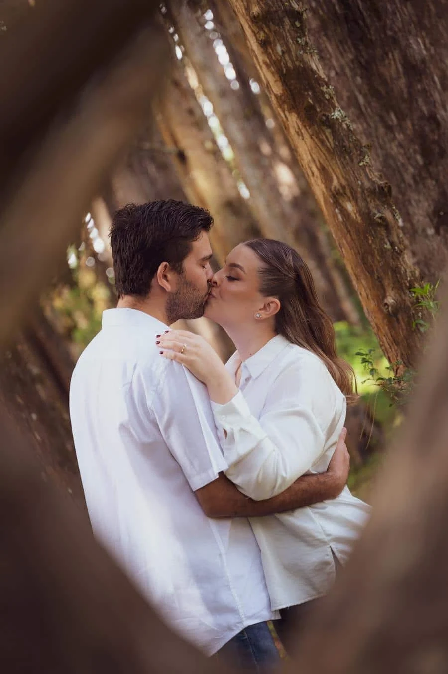 engagement photography costa rica-12 | Pacific Photography Couple sharing a kiss and embracing among tall tree trunks in a forest setting.