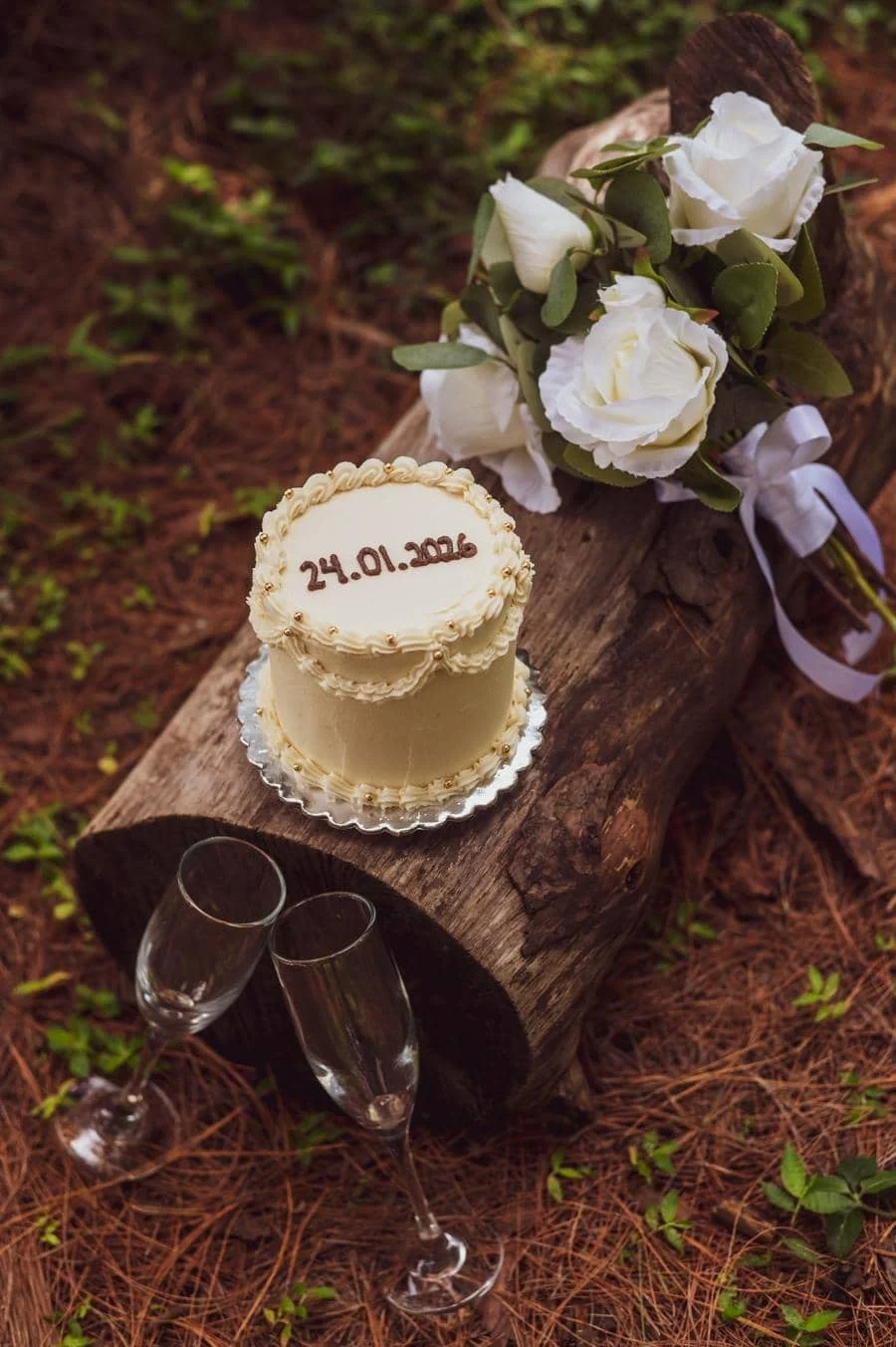 engagement photography costa rica-2 | Pacific Photography Wedding cake with cream frosting and date 24.01.2016 placed on a rustic log beside a white bouquet and two champagne flutes.