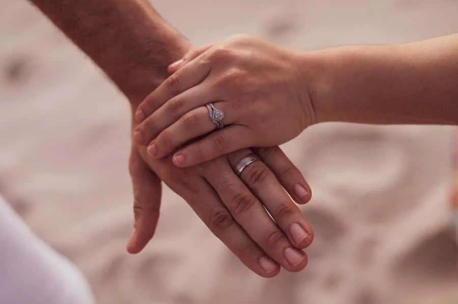 engagement photography costa rica-9 | Pacific Photography Close-up of a couple's hands stacked together, wearing wedding bands, on a sandy background (engagement/wedding scene). Roughly 110 characters