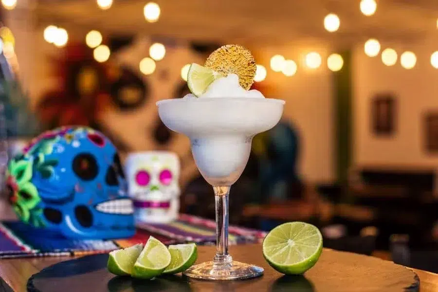 food menu and restaurant photography costa rica -1 | Pacific Photography Margarita on a stemmed glass with a salted rim and lime wedges, festive background with bokeh lights and a colorful skull decoration like Día de los Muertos.