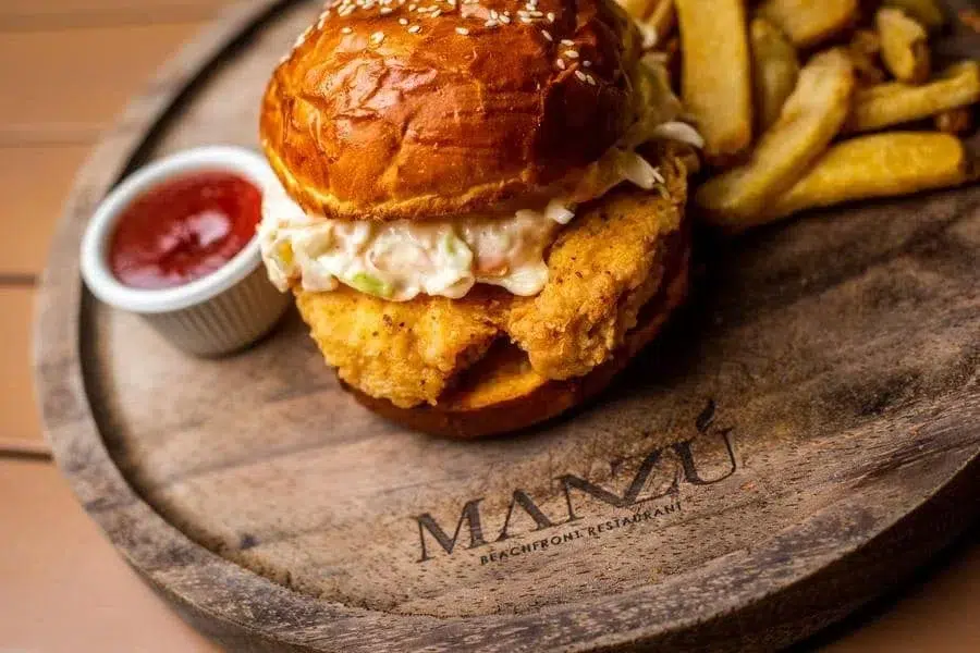 food menu and restaurant photography costa rica -15 | Pacific Photography Crispy fried chicken sandwich with coleslaw on a glossy brioche bun, served with fries and ketchup on a wooden board.