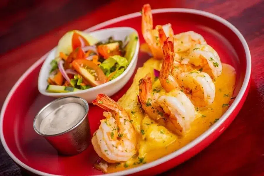 food menu and restaurant photography costa rica -20 | Pacific Photography Shrimp cooked in a creamy yellow sauce, garnished with parsley, served with a side salad and dipping sauce on a red plate.