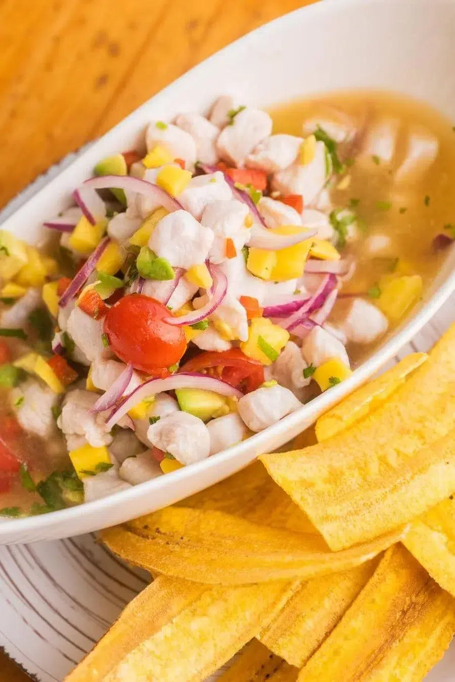 Bowl of fish ceviche with diced mango, red onion, cilantro, and peppers, served with tortilla chips on the side.