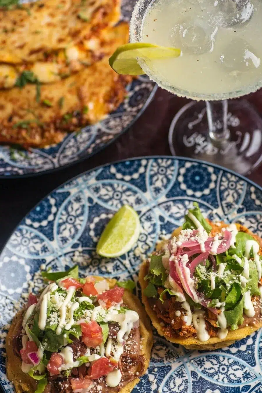 Two loaded tacos on a blue patterned plate with a lime wedge and a margarita glass above them.