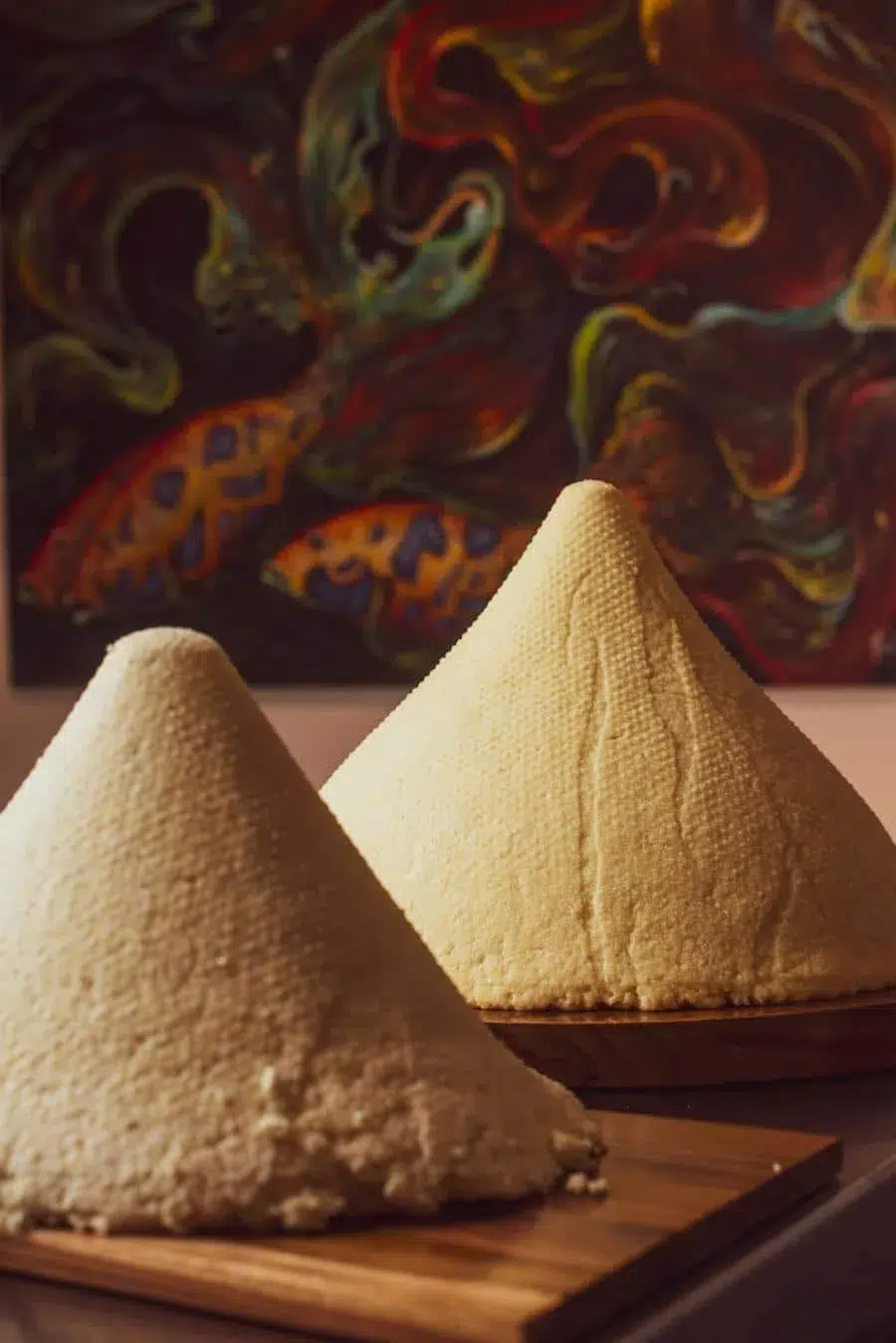 Two pyramid-shaped mounds of rice on wooden boards with a colorful abstract painting in the background.