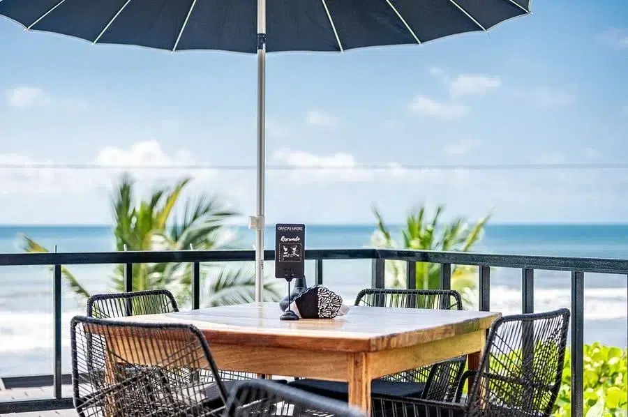 food menu and restaurant photography costa rica -29 | Pacific Photography Outdoor seaside patio with a wooden table, black wicker chairs, and a large blue umbrella overlooking the ocean.