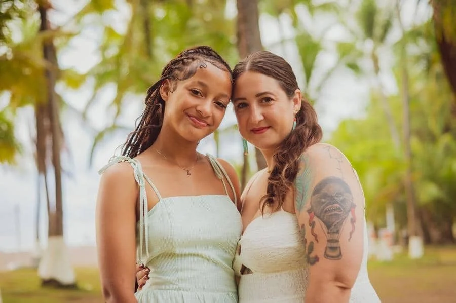 people and lifestyle photography -11 | Pacific Photography Two women pose together outdoors, smiling at the camera in a sunny, palm-lined setting.