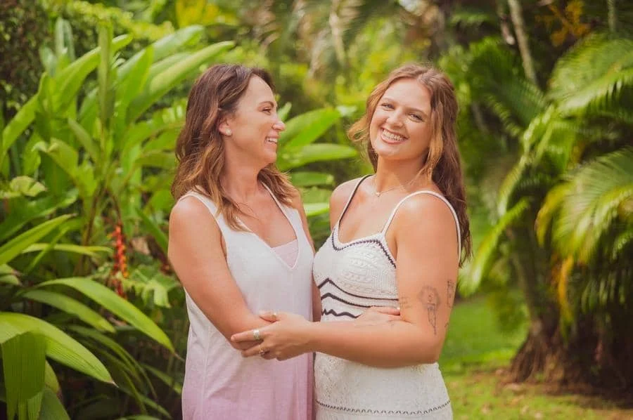 people and lifestyle photography -14 | Pacific Photography Two women in light dresses smile and embrace in a lush garden.