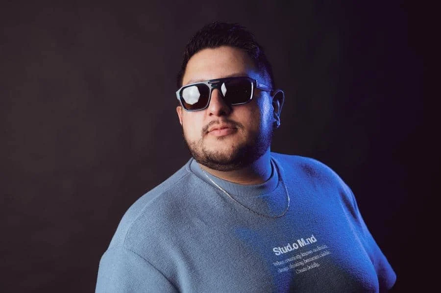 people and lifestyle photography -15 | Pacific Photography Man wearing sunglasses and a blue sweatshirt poses in a dark studio background, looking to the side.