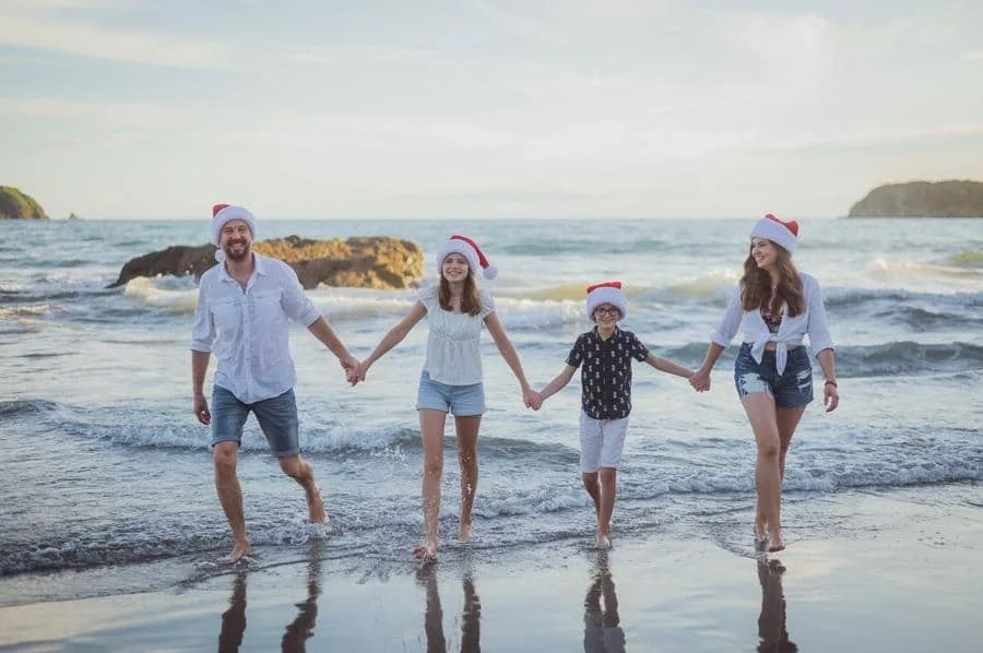 people and lifestyle photography -28 | Pacific Photography Family of four holding hands and walking along the shoreline in Santa hats.