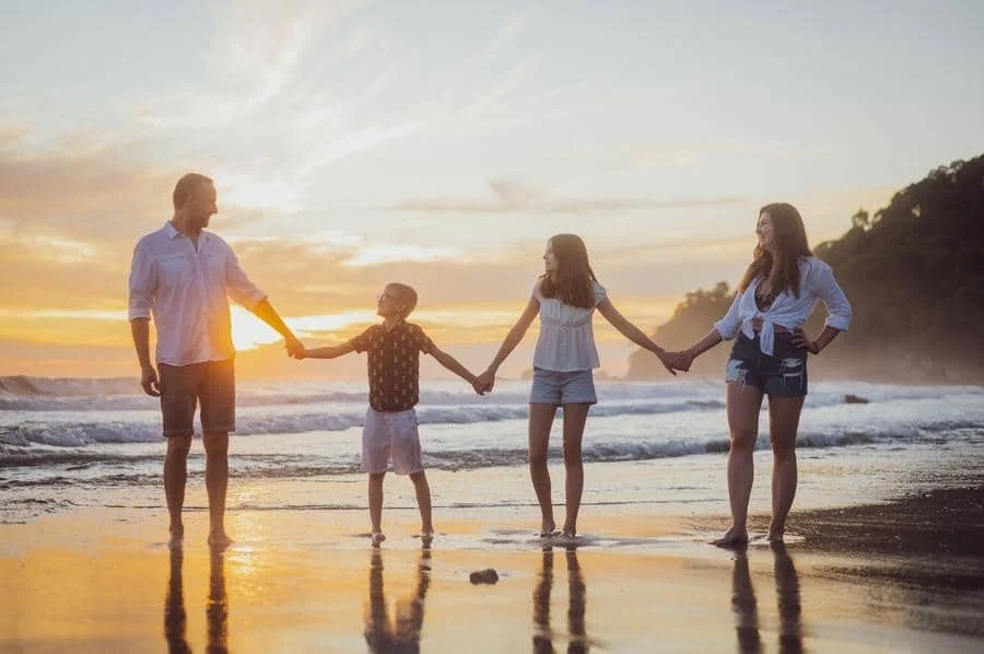 people and lifestyle photography -34 | Pacific Photography A family of four holding hands on a sunny beach at sunset, standing in a line.