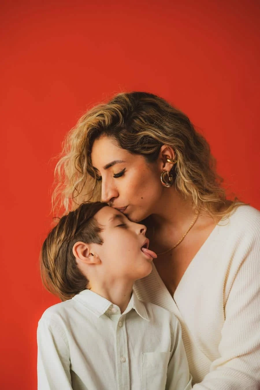 people and lifestyle photography -36 | Pacific Photography Woman kissing a boy on the head against a bright red backdrop.