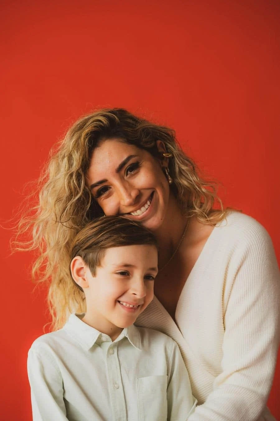 people and lifestyle photography -37 | Pacific Photography Happy woman with curly blond hair and a smiling boy cuddle together against a bright orange background in a warm portrait of a mother and child.
