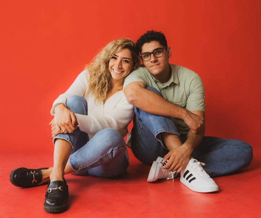 people and lifestyle photography -39 | Pacific Photography Smiling couple sitting on a red studio floor, leaning into each other.�