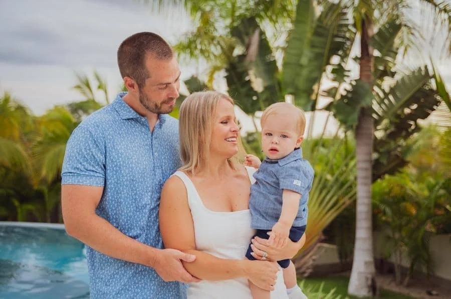 people and lifestyle photography -44 | Pacific Photography A couple with their baby standing by a pool, smiling, surrounded by tropical plants.