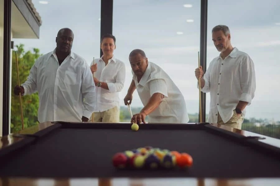 people and lifestyle photography -5 | Pacific Photography Four men in white shirts stand around a pool table, one preparing to shoot a ball as the others watch.