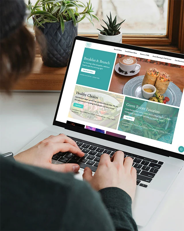person-viewing-website-by-pacific-costa-rica | Pacific Photography Person typing on a laptop displaying a cafe website with sections like Breakfast & Brunch, Healthy Choices, and Green Room Favorites.