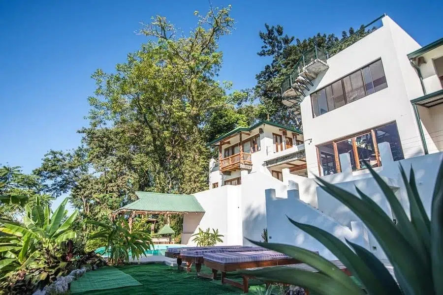 fotografia-para-propiedades-espacios-1 | Pacific Photography Villa moderna blanca con balcones, piscina adyacente y exuberantes plantas tropicales bajo un cielo azul claro.