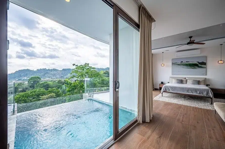 fotografia-para-propiedades-espacios-11 | Pacific Photography Suite de hotel con una cama king, área de estar y puertas corredizas de vidrio a una piscina en el balcón con vista a la ladera.