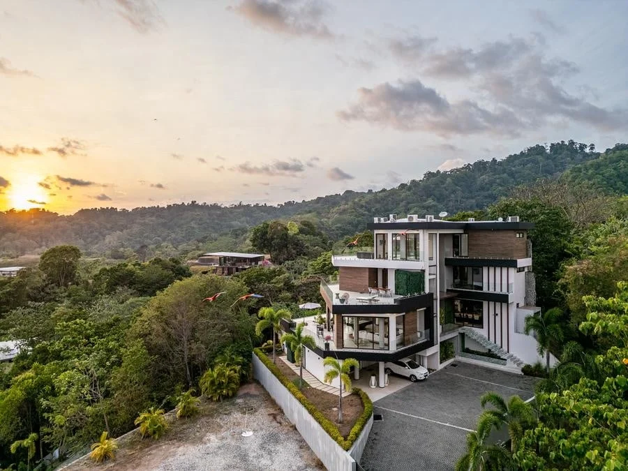 fotografia-para-propiedades-espacios-14 | Pacific Photography Villa moderna de tres pisos en la ladera con balcones, anidada entre árboles tropicales al atardecer.