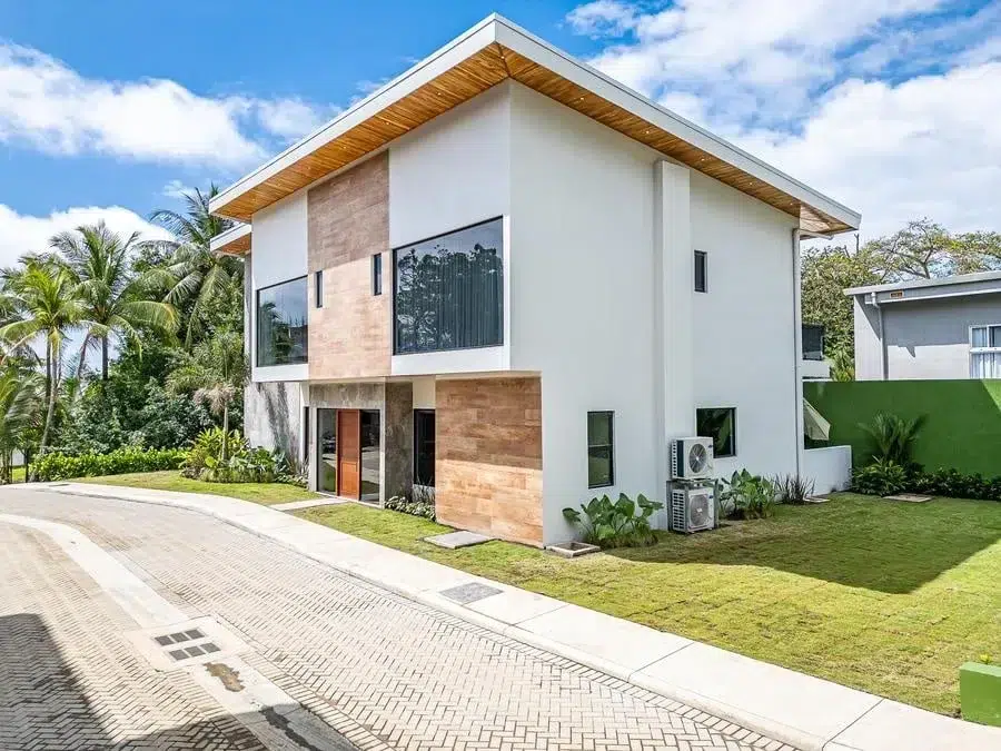 fotografia-para-propiedades-espacios-15 | Pacific Photography Casa moderna de dos pisos con paredes blancas, paneles de acento de madera, grandes ventanales y paisajismo tropical en un día soleado.