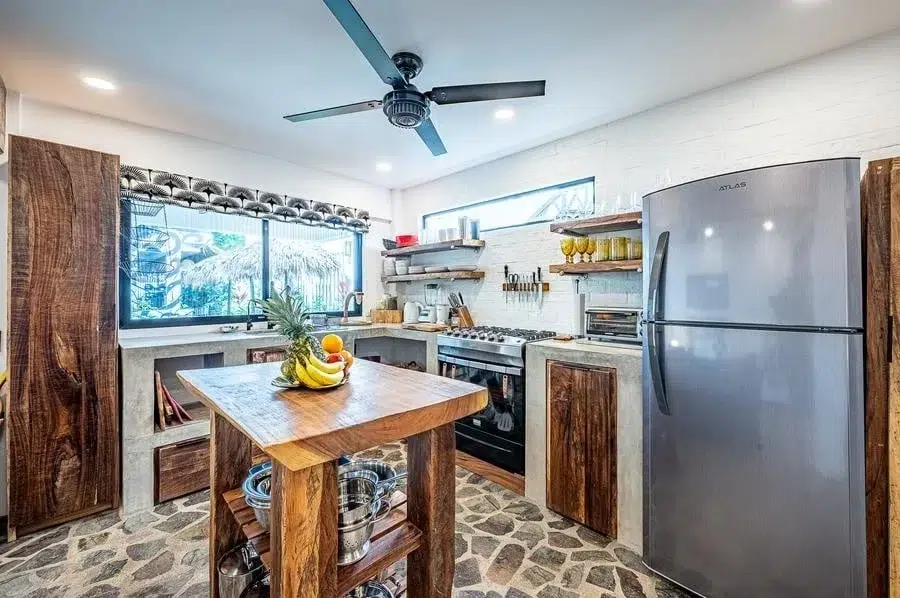 fotografia-para-propiedades-espacios-17 | Pacific Photography Cocina moderna y luminosa con un carrito de isla de madera, frutero, estantes abiertos y un refrigerador de acero inoxidable.