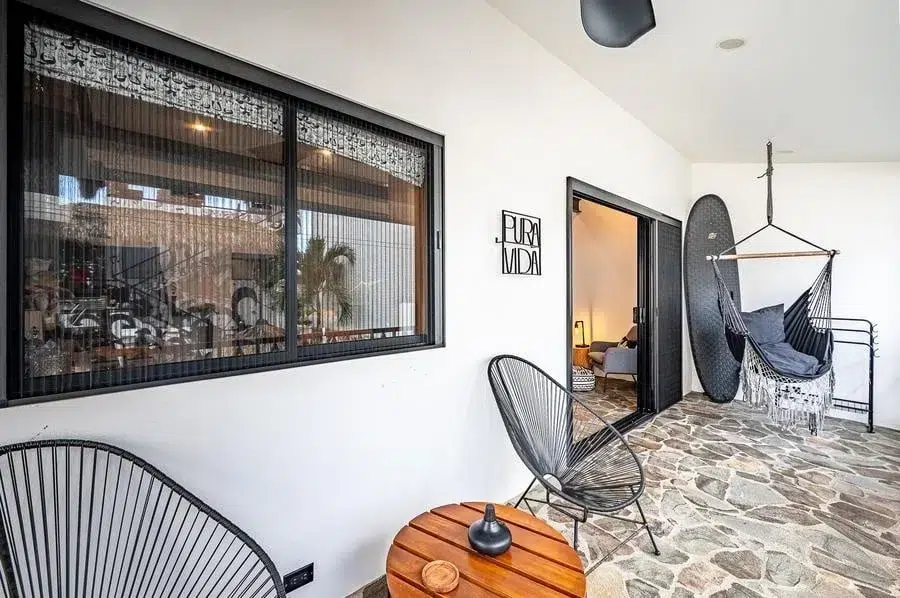 fotografia-para-propiedades-espacios-19 | Pacific Photography Patio exterior con suelo de piedra, sillas de alambre negro, una pequeña mesa redonda y una silla hamaca colgante cerca de una puerta corredera al interior de la casa.