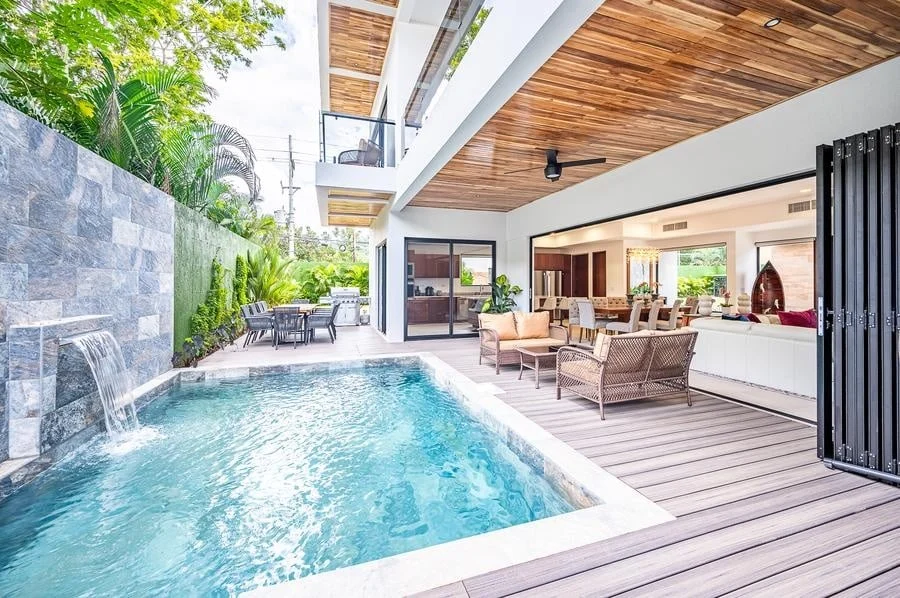 fotografia-para-propiedades-espacios-23 | Pacific Photography Piscina rectangular en el patio trasero con una cascada de piedra, terraza de madera y asientos al aire libre junto a una sala de estar de planta abierta a través de puertas corredizas de vidrio.