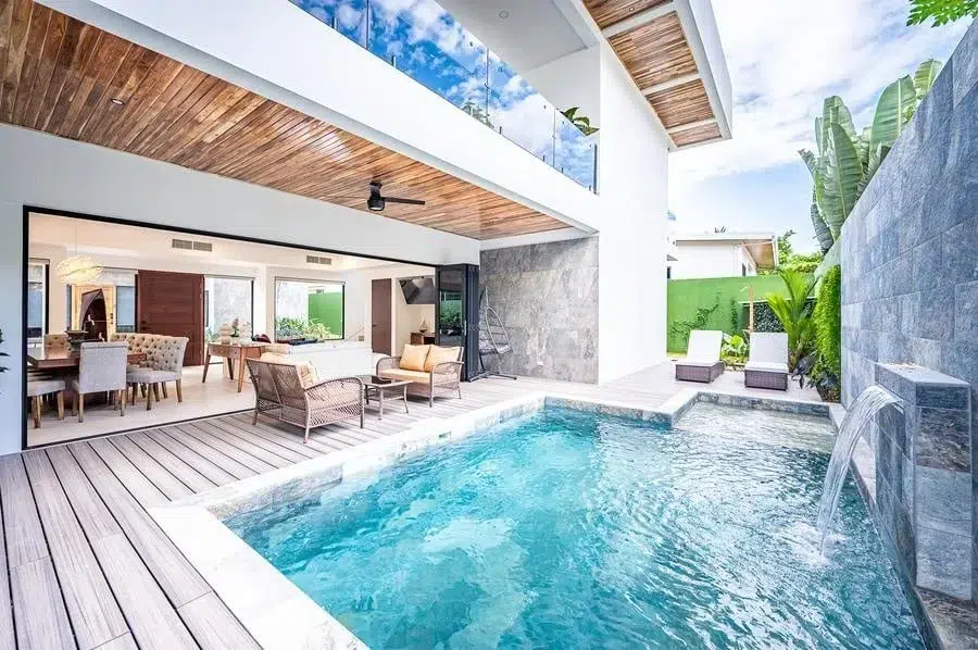 fotografia-para-propiedades-espacios-24 | Pacific Photography Villa moderna con piscina enterrada, terraza de madera y sala de estar abierta que conduce a asientos al aire libre y palmeras.